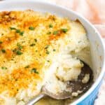 A spoon in a baking dish of a mashed cauliflower casserole with text overlay that says "Whipped Cauliflower".