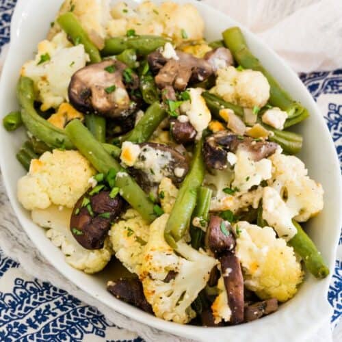 Roasted cauliflower, green beans, and mushrooms with blue cheese in a white oval dish.