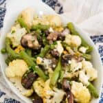 Roasted cauliflower, green beans, and mushrooms in an oval serving dish with text overlay that says "Blue Cheese Roasted Vegetables".