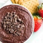 A bowl of dark chocolate hummus topped with chopped chocolate with graham and strawberries for dipping.