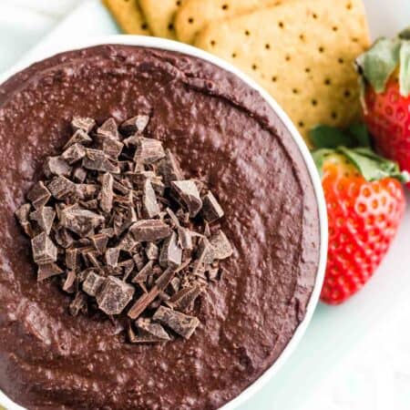 A bowl of dark chocolate hummus topped with chopped chocolate with graham and strawberries for dipping.