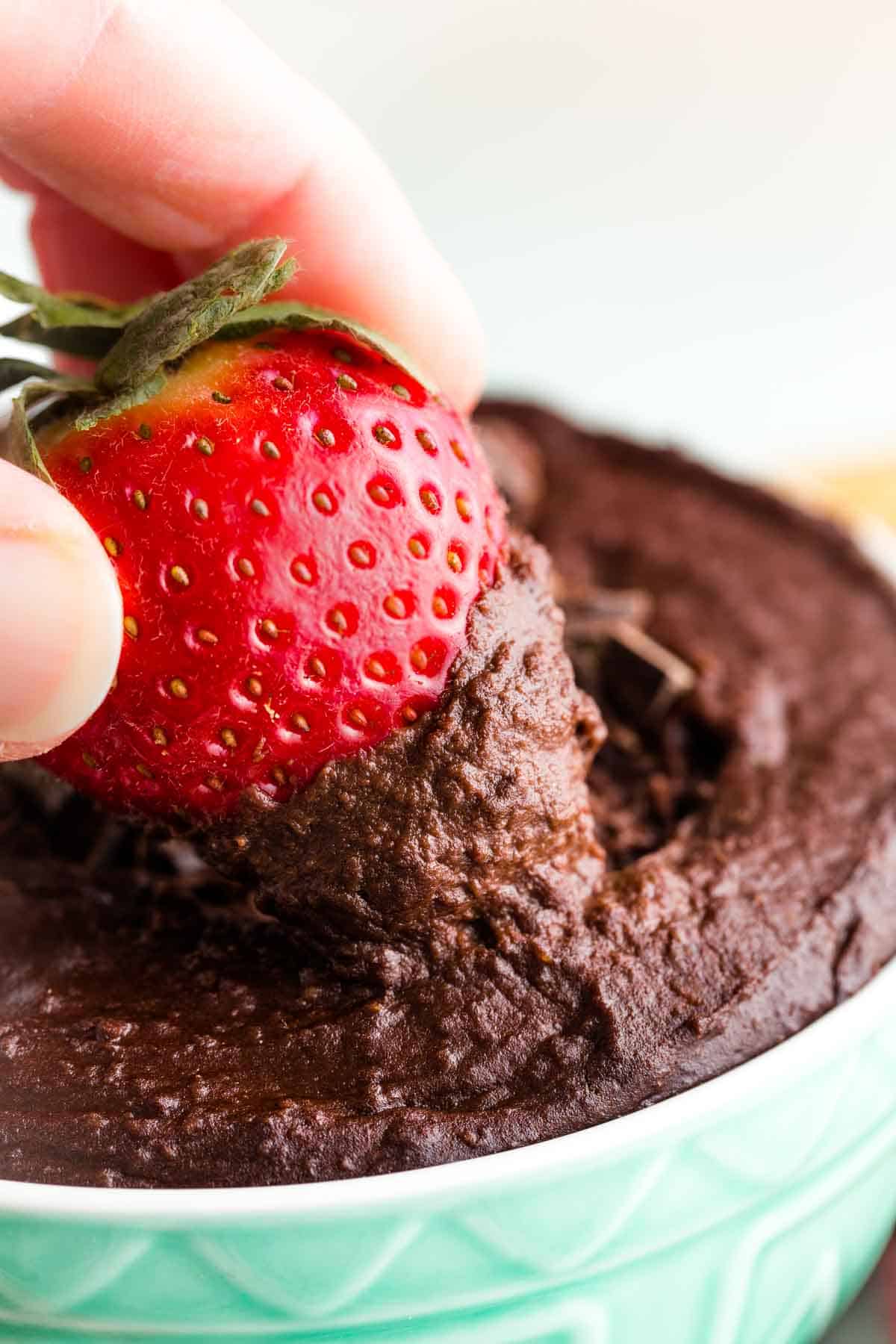 A close up of a strawberry dipped in dark chocolate hummus.