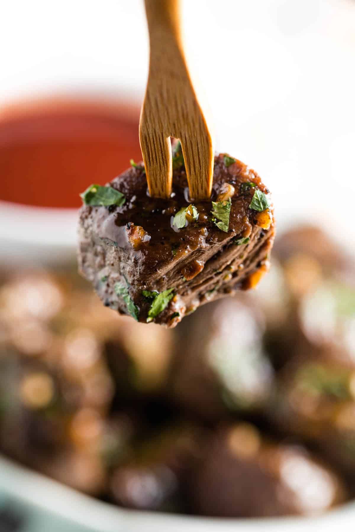 A cubed piece of a steak bite is held by a toothpick.