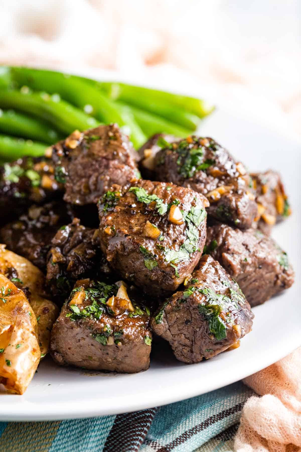 Steak bites are served on a white plate with green beans.