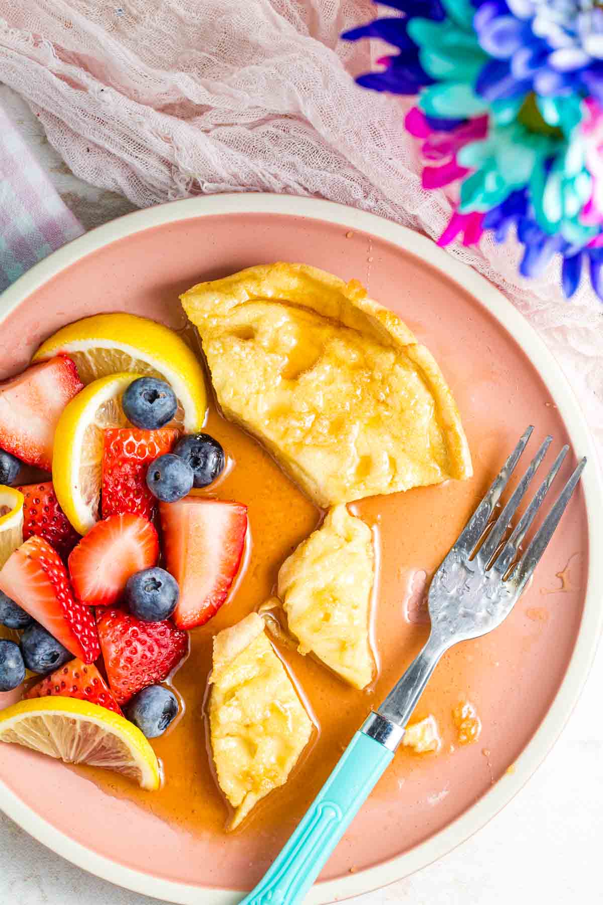 Fruit and German pancakes are served on a pink plate with a fork.