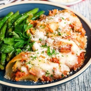 A plate of stuffed shells covered with mozzarella and parmesan on a blue plate with green beans.