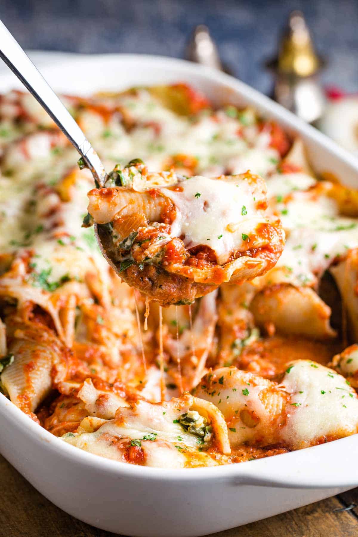 A portion of spinach stuffed shells is lifted out of the pan.