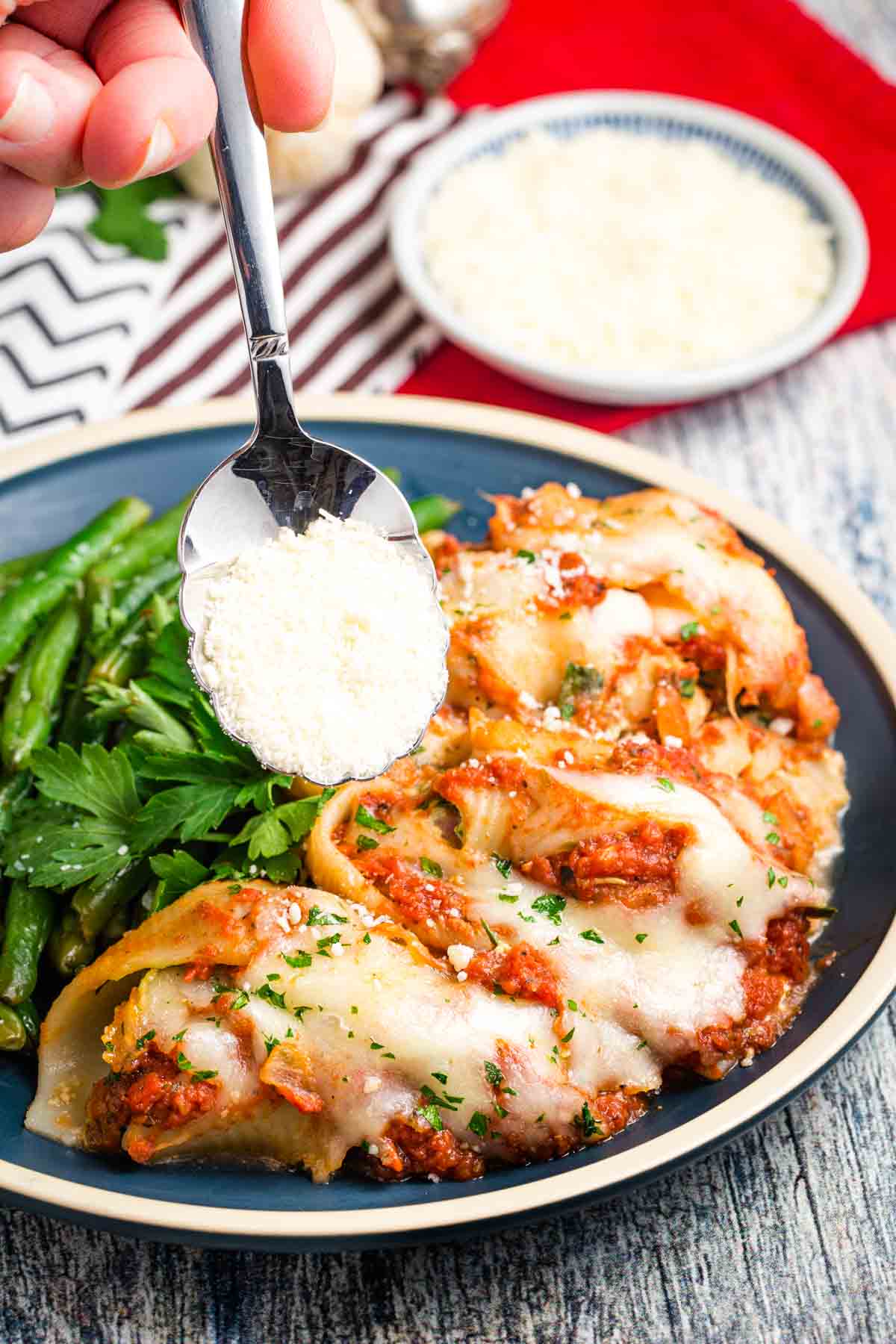 A spoon drizzles parmesan over a plate of spinach stuffed shells.