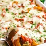A serving spoon scooping up a stuffed shell covered with mozzarella and parmesan out of a casserole dish with text overlay that says "Ham and Spinach Stuffed Shells".