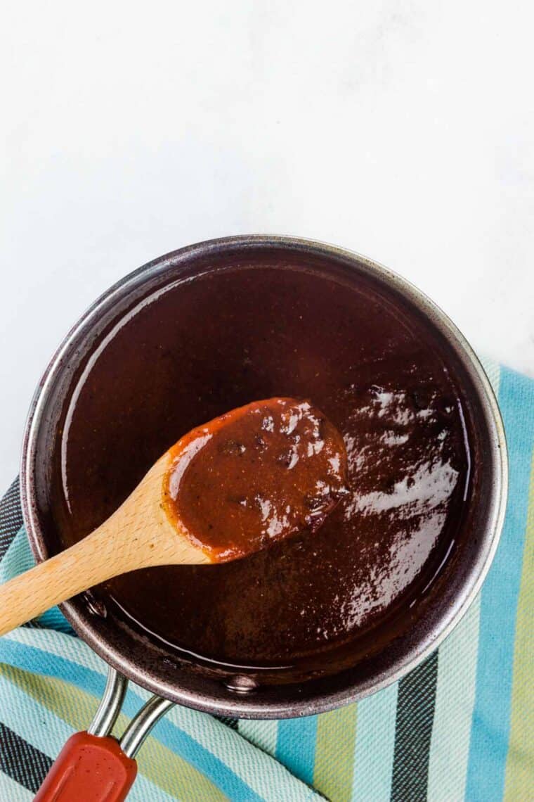 The smooth, dark sauce is mixed with a wooden spoon.