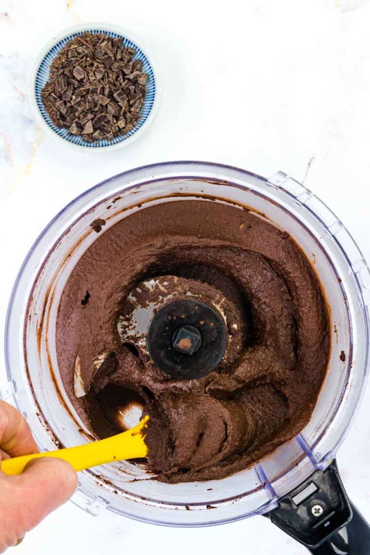 A spatula scrapes down the bowl of a food processor for dark chocolate hummus.