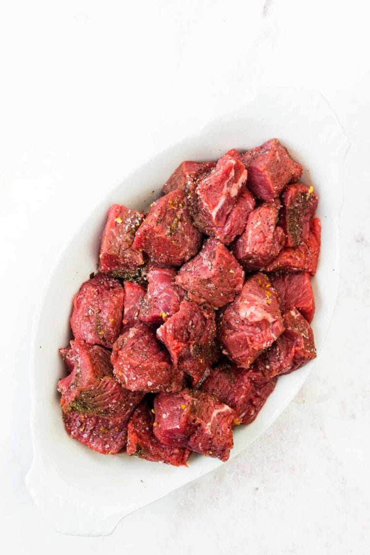 A white dish holds cubes of seasoned steak.