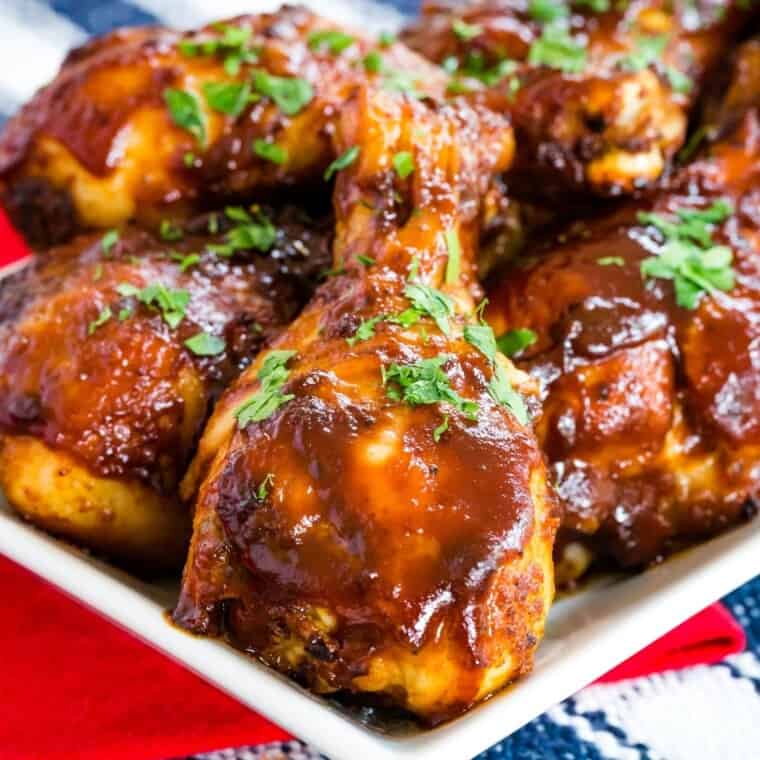 Chicken drumsticks coated in barbecue sauce on a white plate.