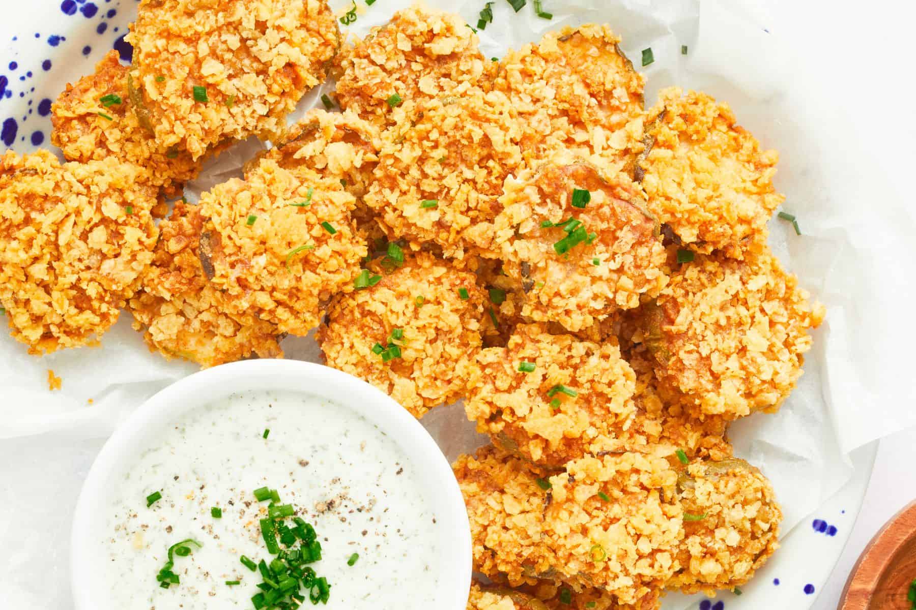 Potato chip-crusted fried pickles on a parchment-lined platter with a bowl of dip.