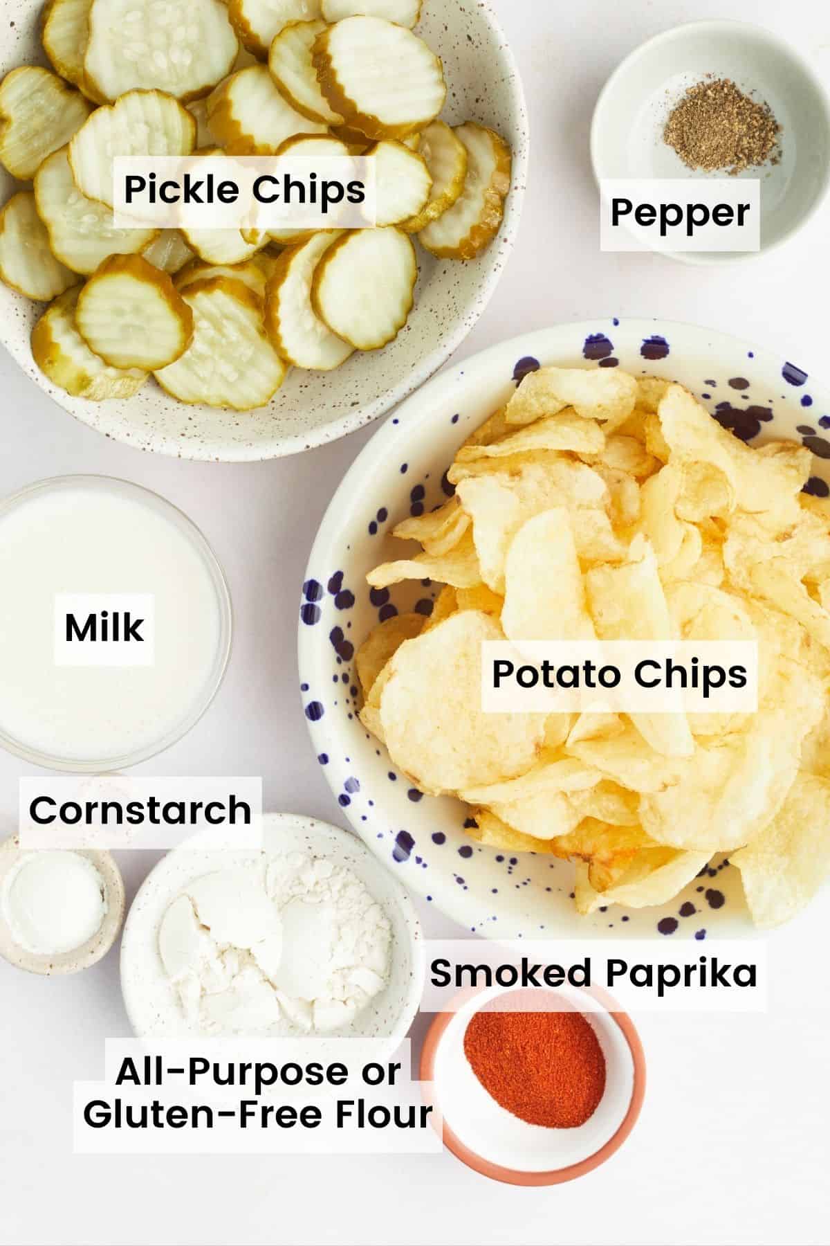 The ingredients for air fryer fried pickles are shown portioned out with text labels: pickle slices, potato chips, gluten free flour, cornstarch, paprika, milk, pepper.