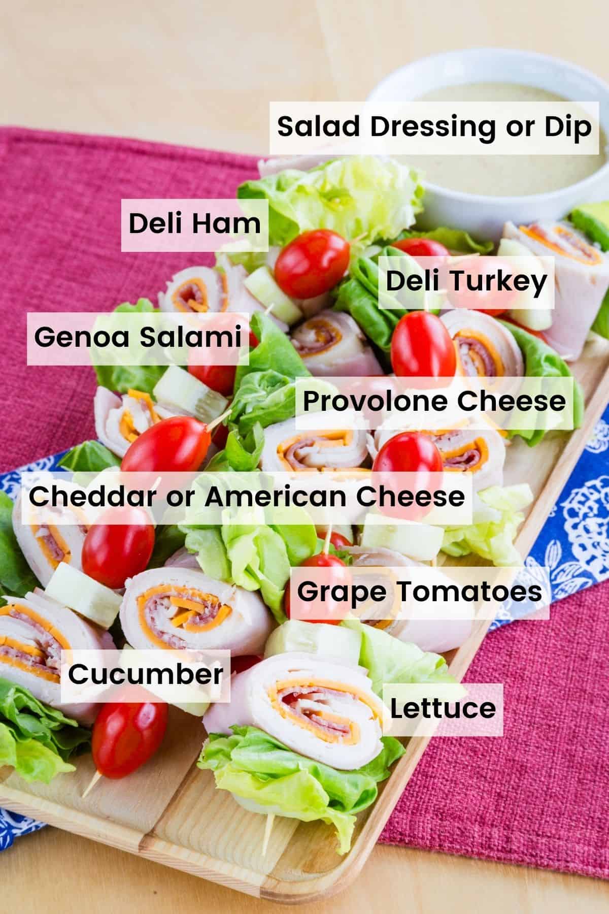 A platter of chef salad on a stick skewers with text labels of the ingredients including: Salad dressing or dip, Deli Ham, Deli Turkey, Genoa Salami, Provolone Cheese, Cheddar or American Cheese, Grape Tomatoes, Cucumber, and Lettuce.