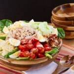 A Cobb salad topped with chicken, tomatoes, cucumber, hard boiled eggs, and more, in a bowl.