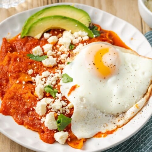 A plate of Chilaquiles Rojos topped with a fried egg and cotija cheese.
