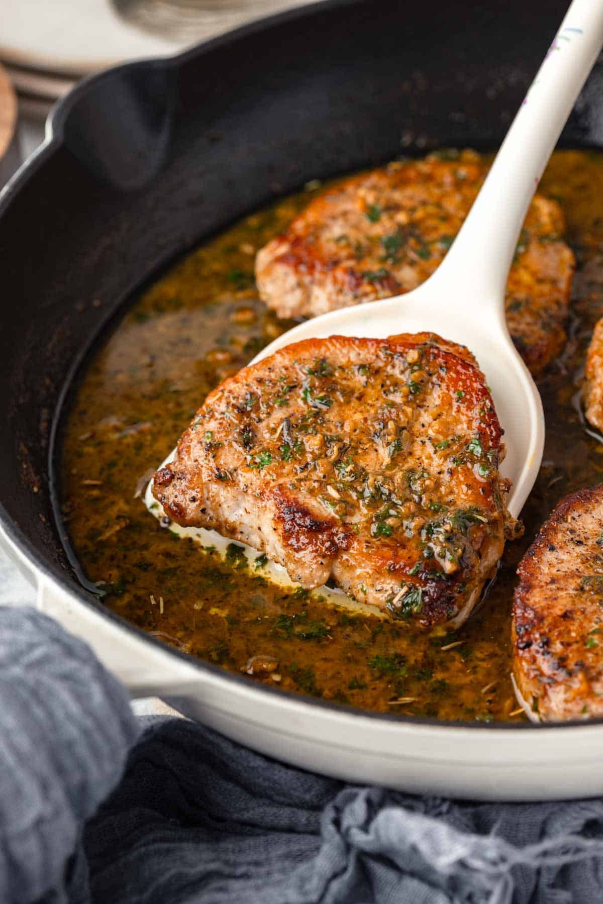 A spatula lifts a garlic butter pork chop out of the skillet.