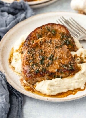 Sauce drips into a pile of mashed potatoes topped with a garlic butter pork chop.