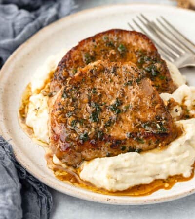 Sauce drips into a pile of mashed potatoes topped with a garlic butter pork chop.