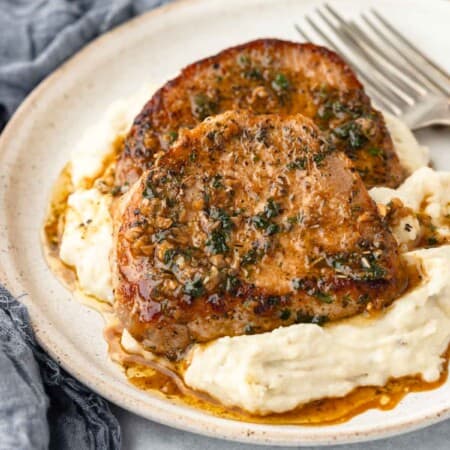 Sauce drips into a pile of mashed potatoes topped with a garlic butter pork chop.