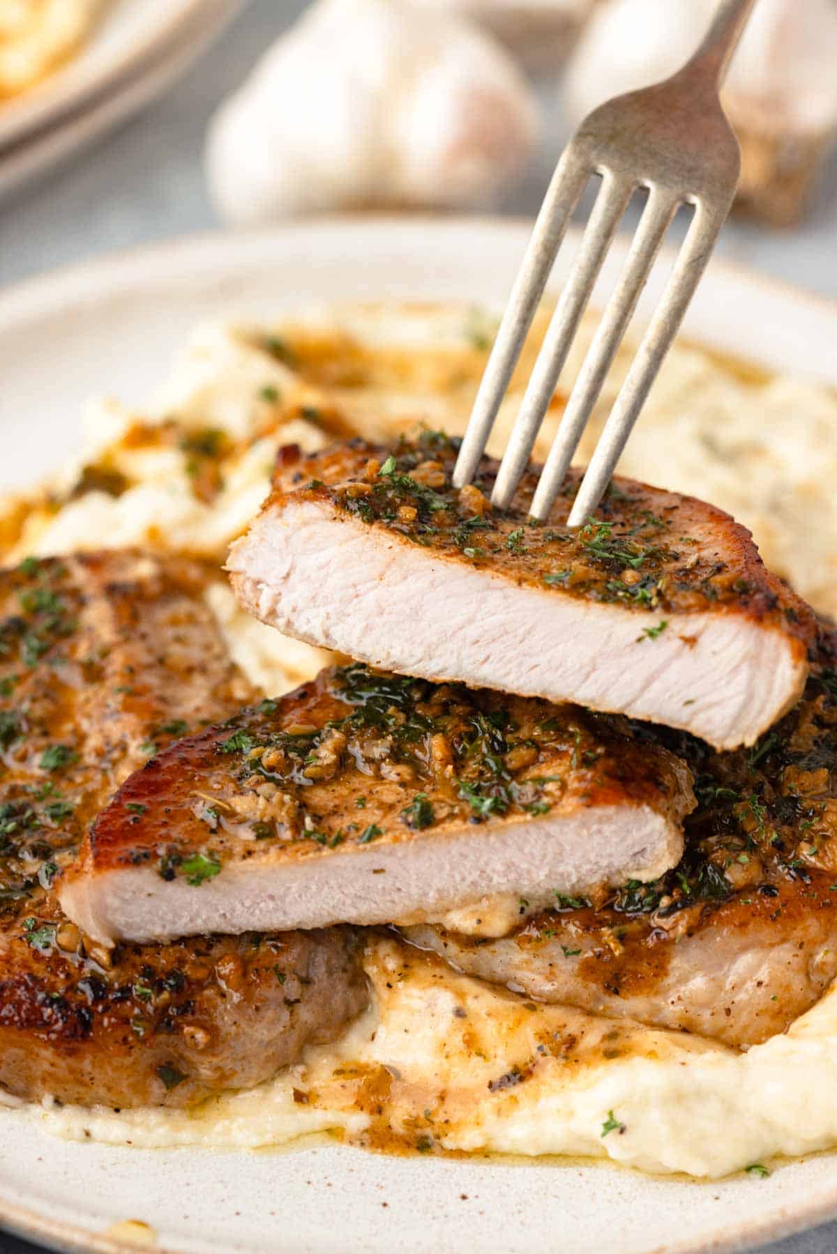 A fork picks up a bite of a piece of garlic butter pork chops.