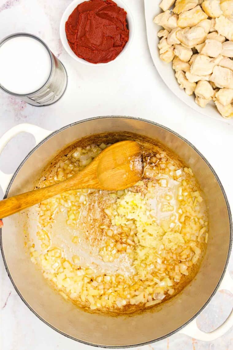 Garlic is stirred into a pot with a wooden spoon.