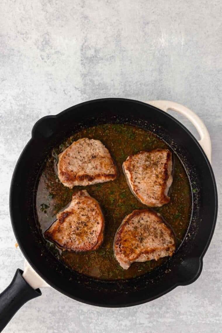 The seared pork chops are added back to the skillet.