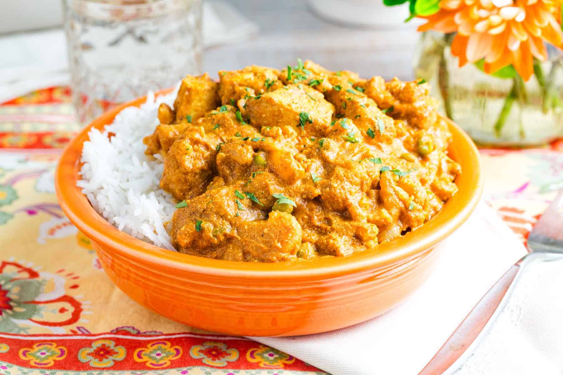 An orange bowl holds a serving of white rice topped with quick chicken curry.