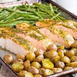 A sheep pan with green beans, small potatoes, and salmon filets covered with pesto.