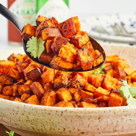 A spoonful of roasted sweet potato cubes being held over a bowl of them.