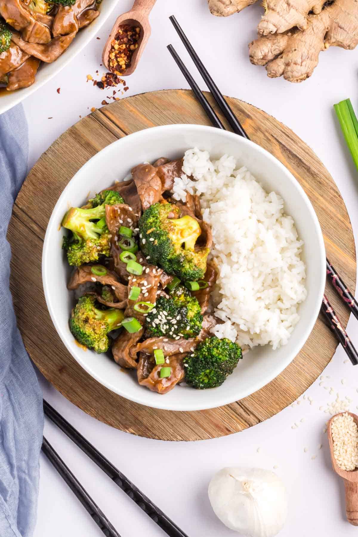 A bowl of beef and broccoli served over white rice with chopsticks on the side.