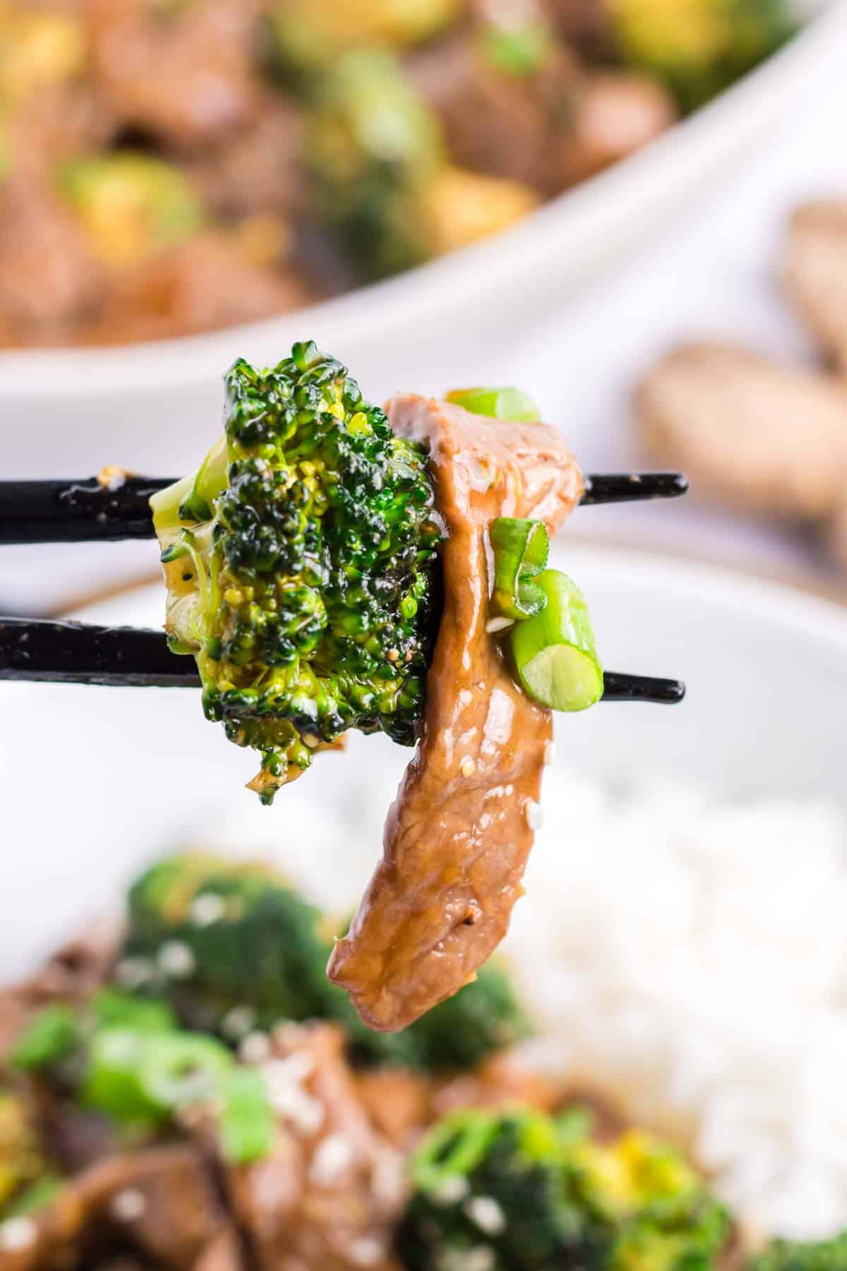 A piece of broccoli and a piece of beef strip are picked up by chopsticks.