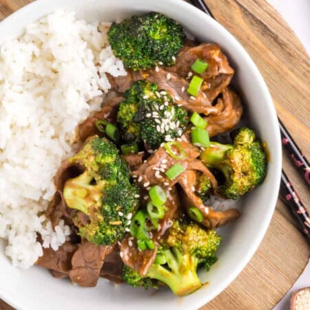 A bowl contains half white rice and half beef and broccoli stir fry.