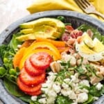 A plate of spinach salad with a variety of toppings with text overlay that says "Strawberry Spinach Salad".