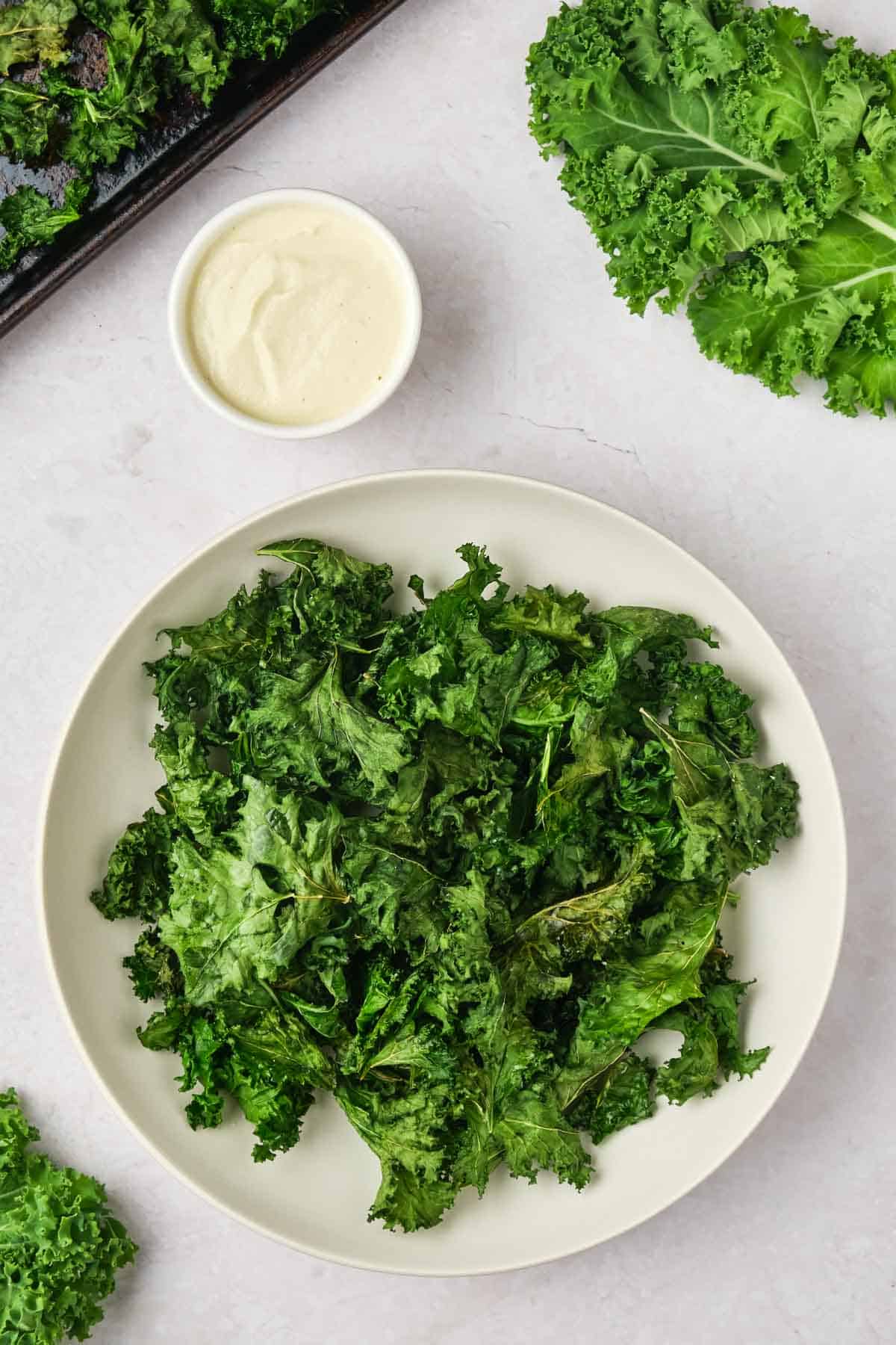 Kale, a bowl of kale chips, and a bowl of sauce.