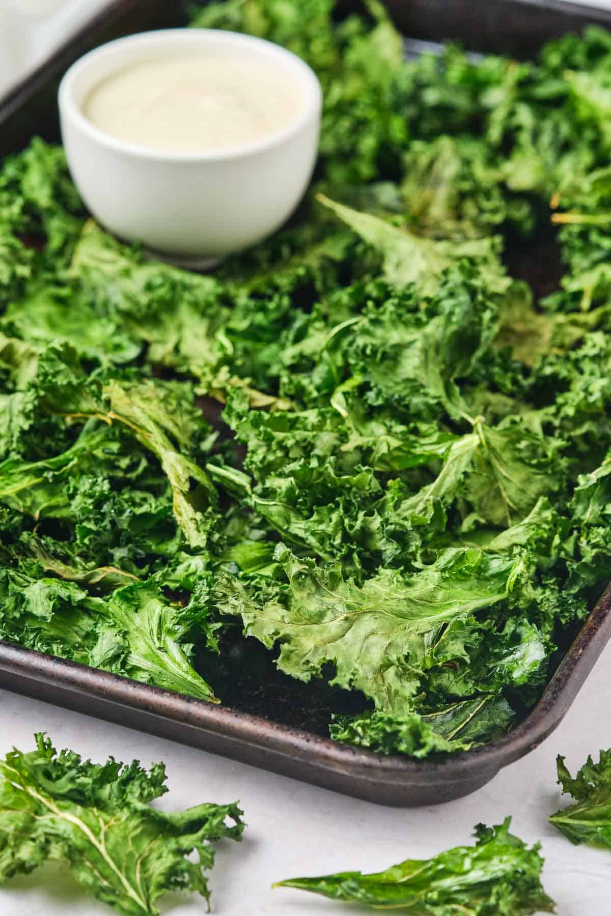 A tray holds air fryer kale and a bowl of sauce.