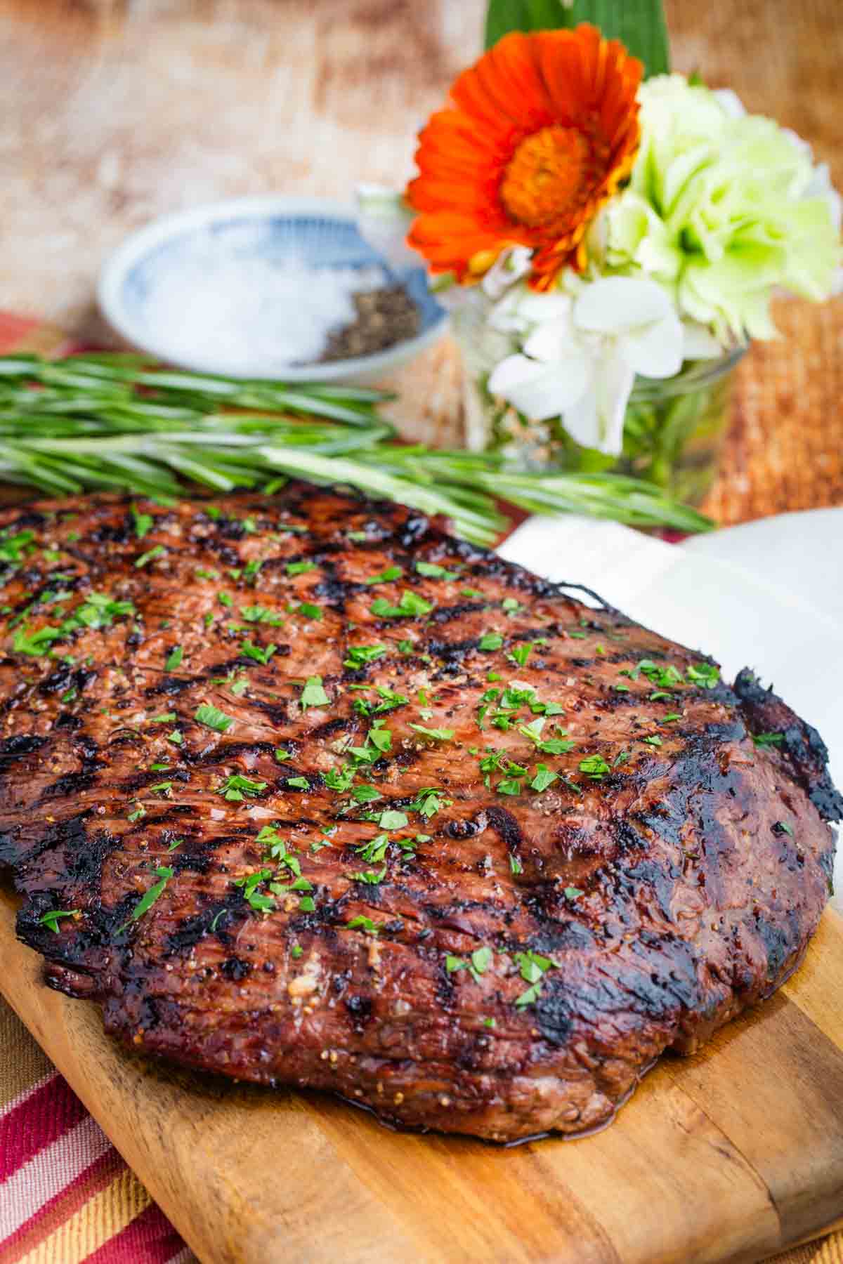 A whole grilled flank steak rests on a wooden cutting board.