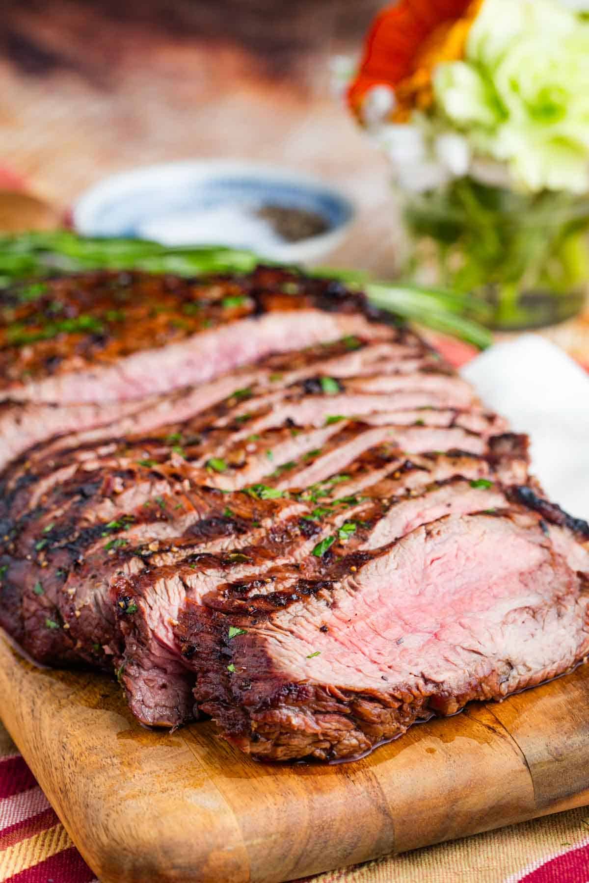 A cutting board holds thin slices of balsamic marinated flank steak.
