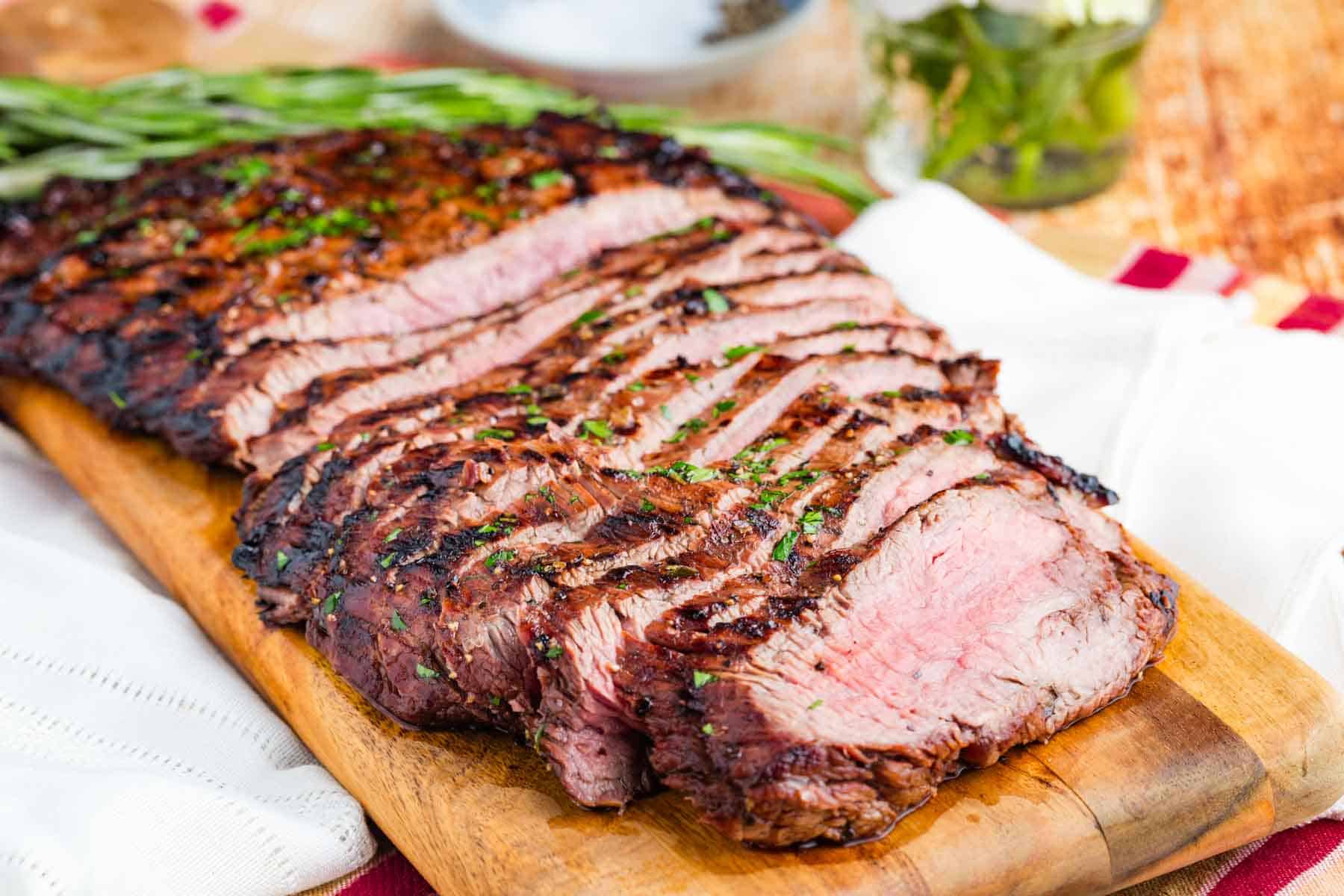 A cutting board holds thin slices of balsamic marinated flank steak.