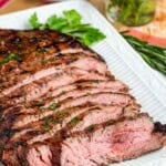 Slices of juicy grilled flank steak on a white serving platter.