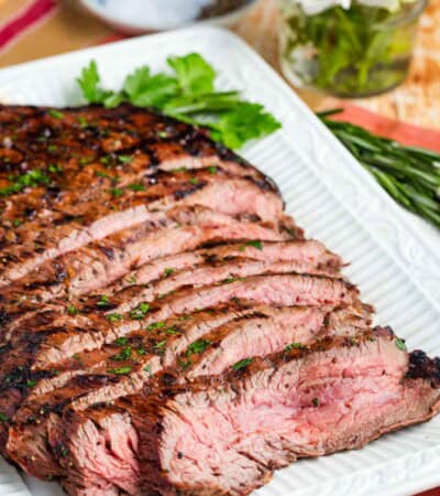 Slices of juicy grilled flank steak on a white serving platter.