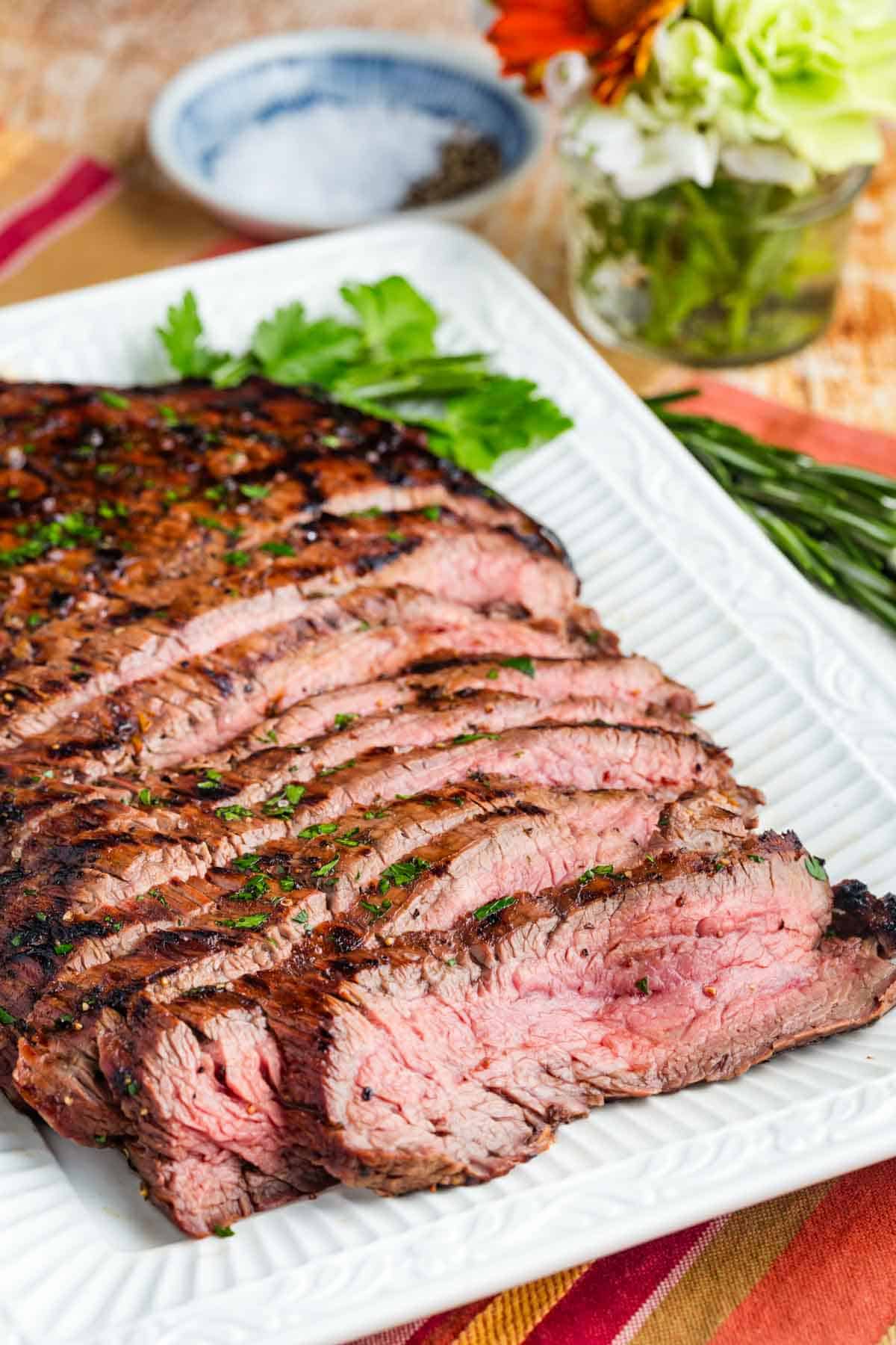 Slices of juicy grilled flank steak on a white serving platter.