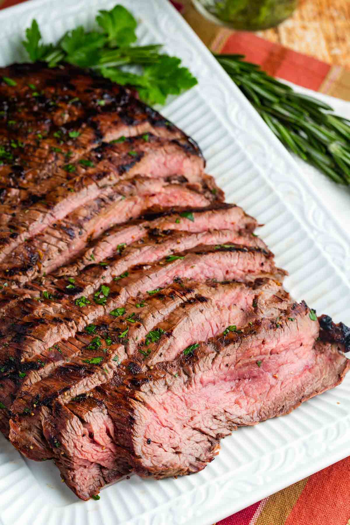 A grilled flank steak is served in slices on a white platter.