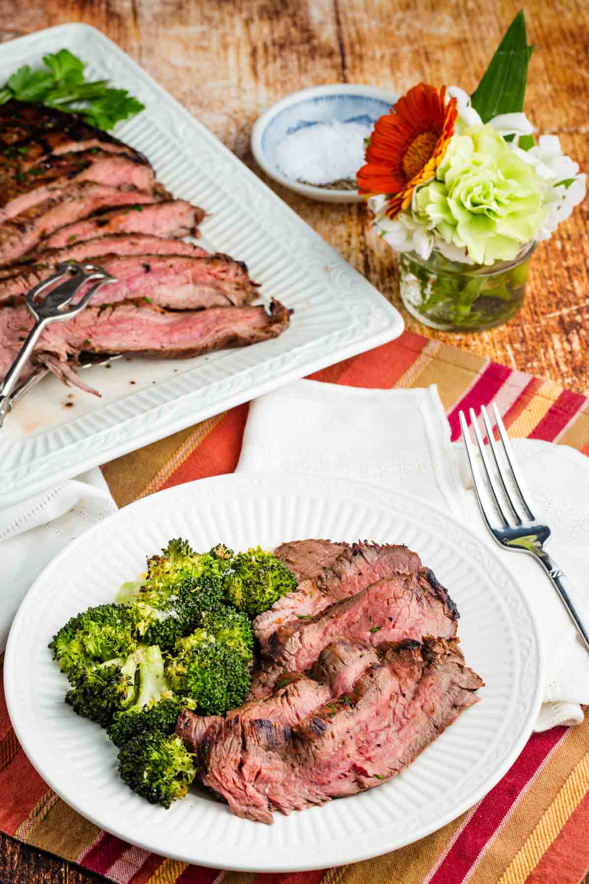 Slices of balsamic marinated flank steak are served with broccoli on a plate.