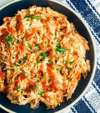 A bowl of crockpot bbq chicken on a table with a plaid background.