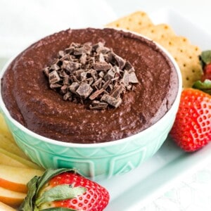 A bowl of dark chocolate hummus on a platter of strawberries, apple slices, and graham crackers.