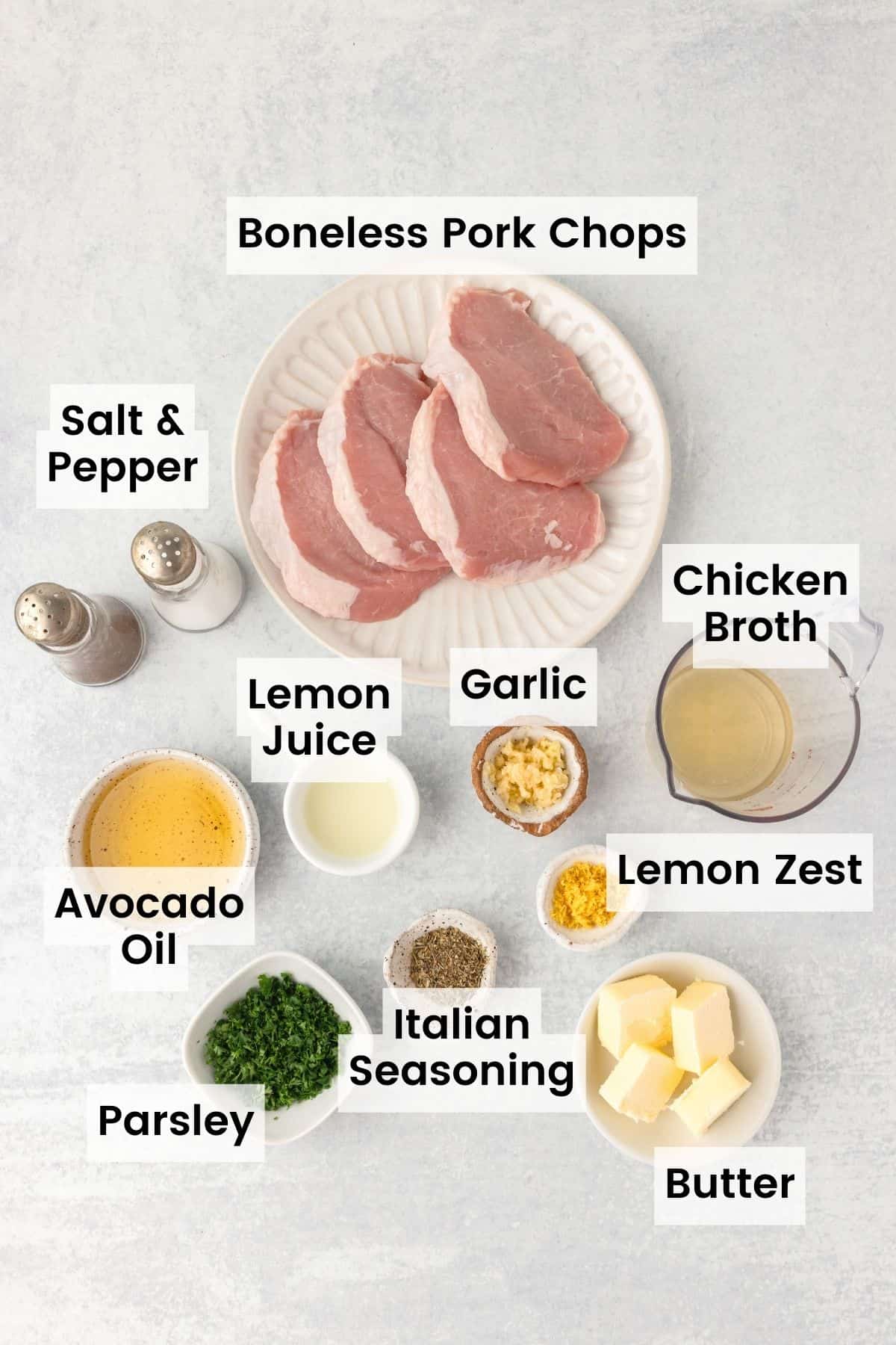 Ingredients for garlic butter pork chops are shown portioned out with text labels: pork, garlic, butter, parsley, salt and pepper, parsley, oil.