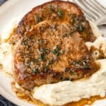 Two pork chops covered in sauce served on top of mashed potatoes with text overlay that says "Garlic Butter Pork Chops".